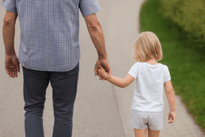 Un uomo adulto tiene per mano una bambina mentre camminano lungo un sentiero, simbolo di protezione e fiducia, tema dell’articolo “Non parlare con gli sconosciuti”.